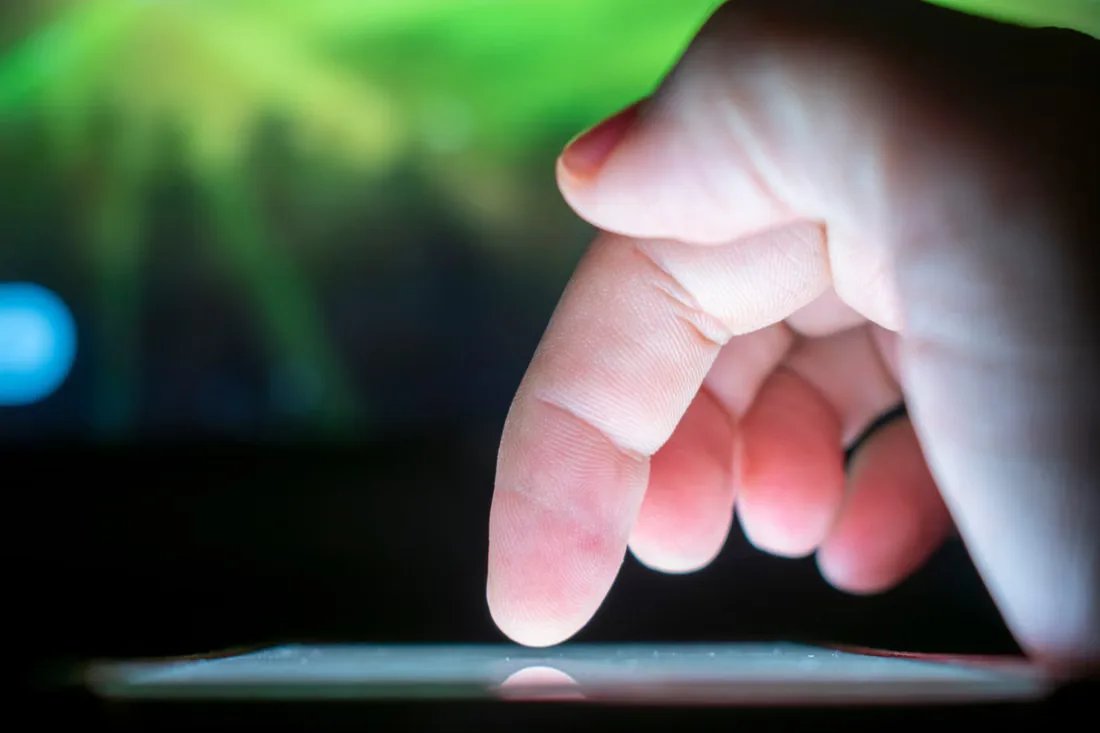 A finger reaching down to touch an illuminated tablet screen